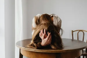 mujer recostada en una mesa, abrazandose la cabeza con las manos
